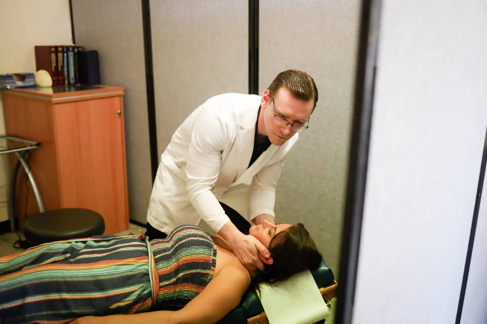 Dr. Michael Brandon adjusting the neck of a patient lying face up on a treatment table at FIT Clinic in Colts Neck
