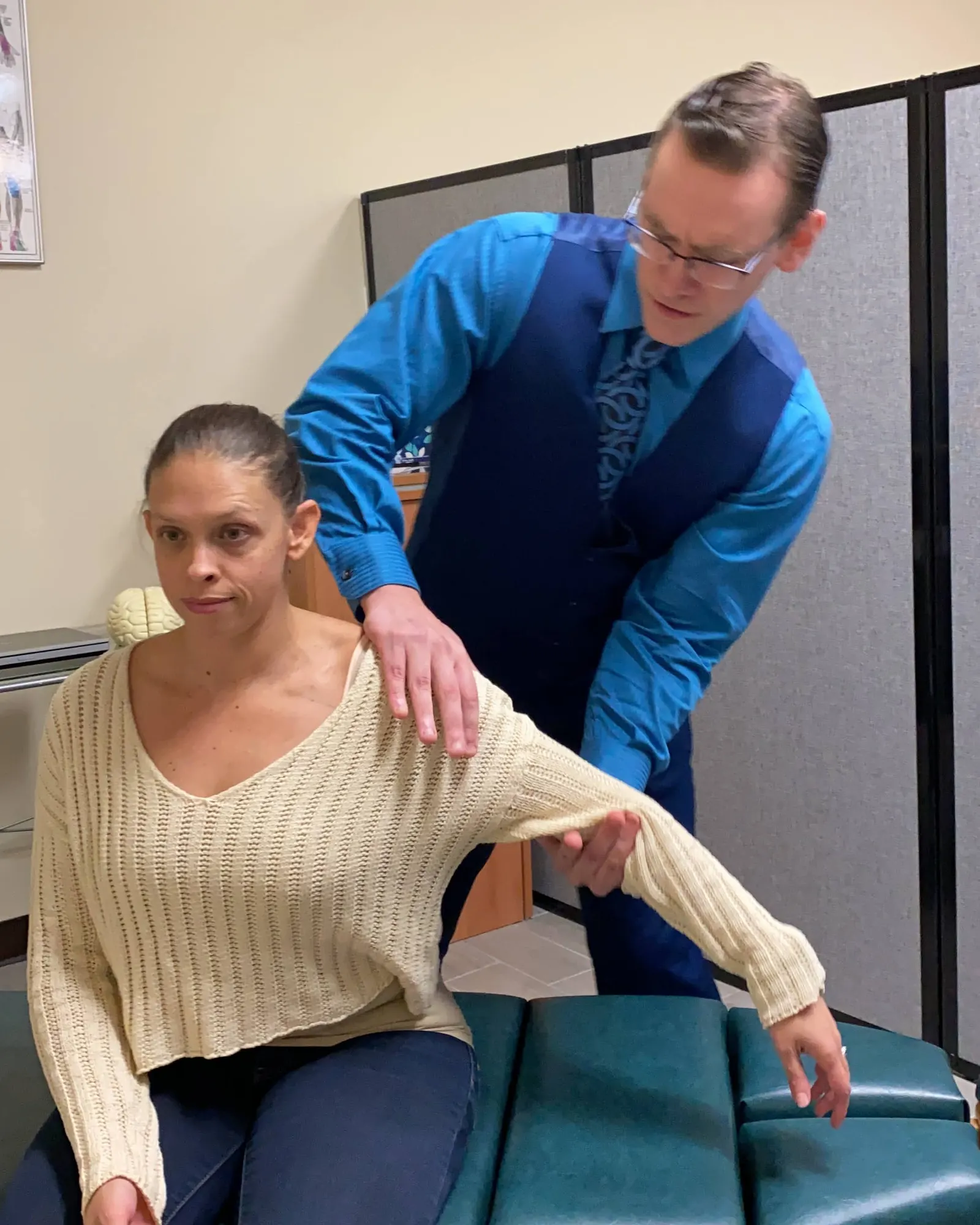 Dr. Michael Brandon guiding a seated patient's arm to check how her shoulder moves at FIT Clinic in Colts Neck