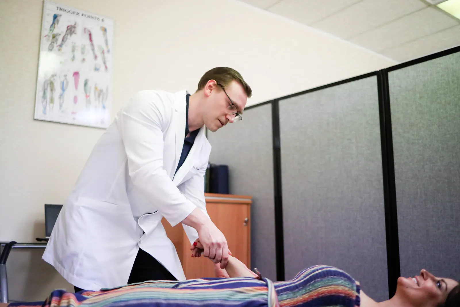 Dr. Michael Brandon checking the wrist of a patient lying on a treatment table at FIT Clinic in Colts Neck