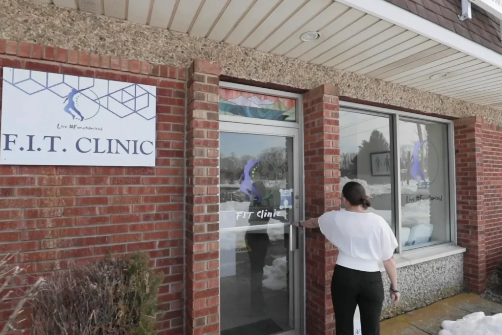 A visitor opening the glass front door of FIT Clinic in Colts Neck, below the clinic's wall sign