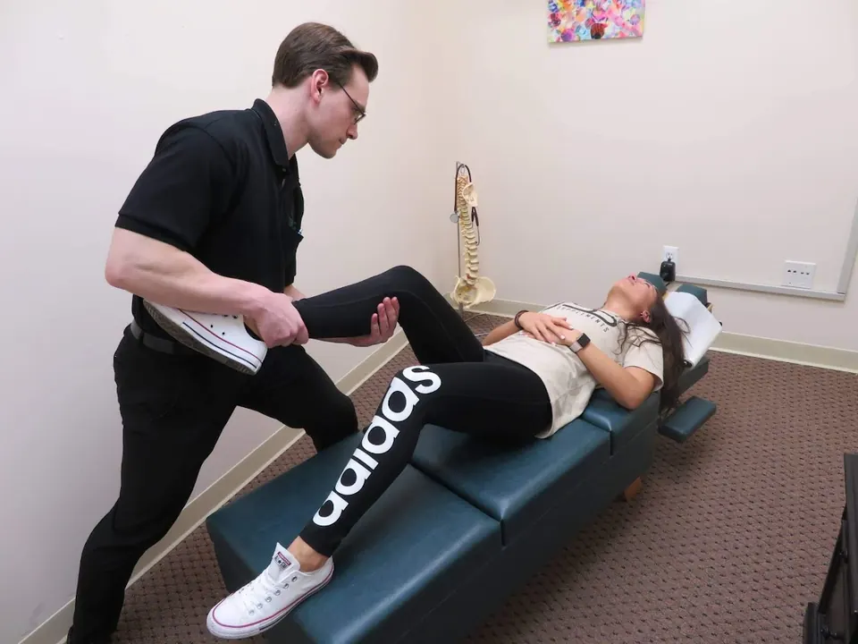 Dr. Michael Brandon raising a patient's straight leg to stretch the back of her thigh on a treatment table